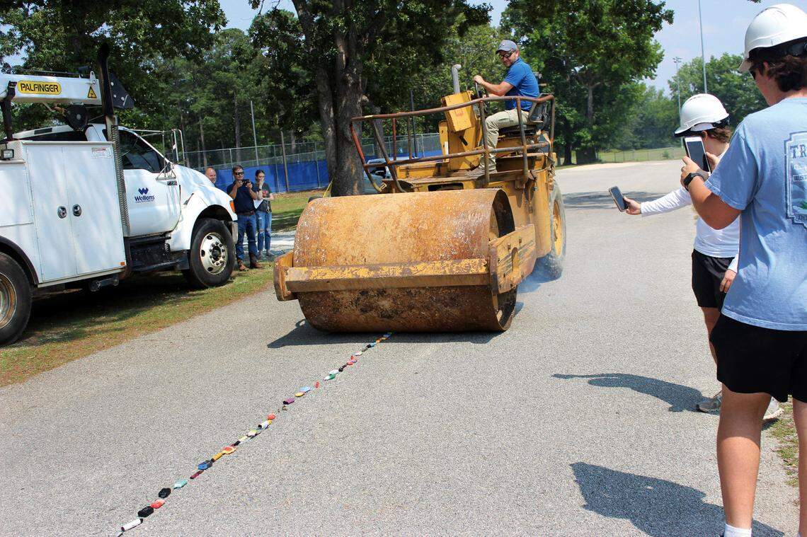 Jason Thomason, of Wellons Construction, rolls over a line of vaping devices with a steel drum roller near the baseball field at Triton High School. Micheal Cole and Hunter Thompson, at right, record a video of the destruction.