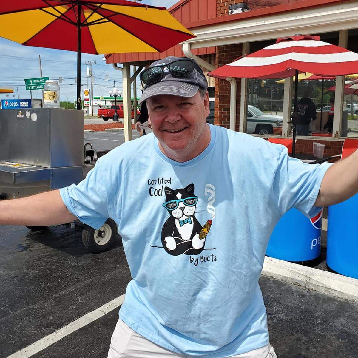 Donnie Douglas, retired editor and current columnist for The Robesonian in Lumberton, shows off the T-shirts featuring his cat Boots, whose witty vignettes have made him a local celebrity.