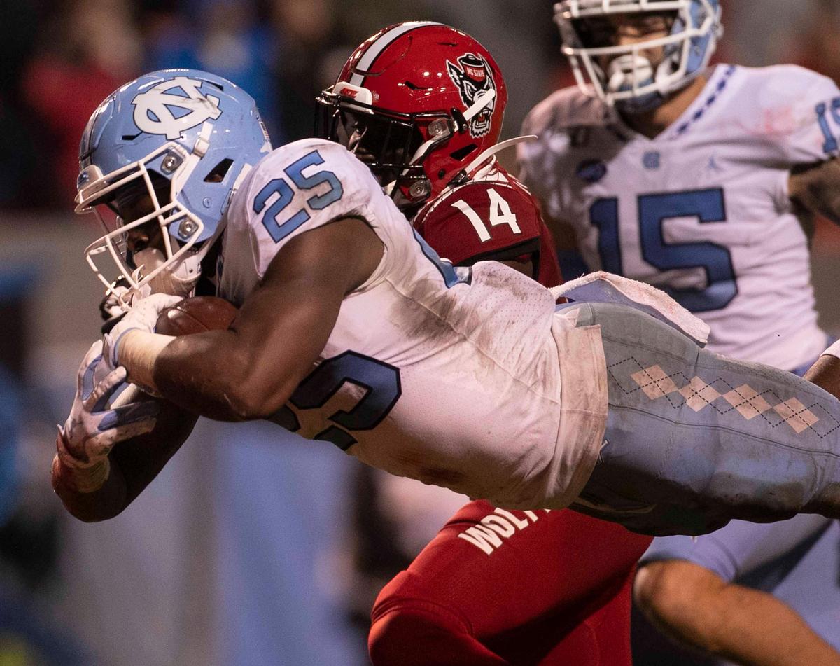 North Carolina’s Javonte Williams (25) dives into the end zone ahead of N.C. State’s De’Von Grave (14) on a 26 yard carry to put the Tar Heels up 13-10 in the third quarter against N.C. State on Saturday, November 30, 2019 at Carter-Finley Stadium in Raleigh, N.C.