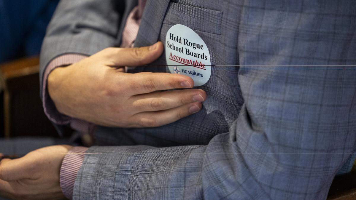 A member of the audience adjusts a sticker on their coat during the questioning of Chapel Hill-Carrboro City Schools Superintendent Rodney Trice and School Board Chair George Griffin during a sometimes tense N.C. House committee hearing on Wednesday, Dec. 10, 2025, in the Legislative Building auditorium in Raleigh. Griffin apologized to the committee Wednesday for not being clearer about his comments on the Parents’ Bill of Rights amid a barrage of questions and accusations about “woke” learning in the classroom.