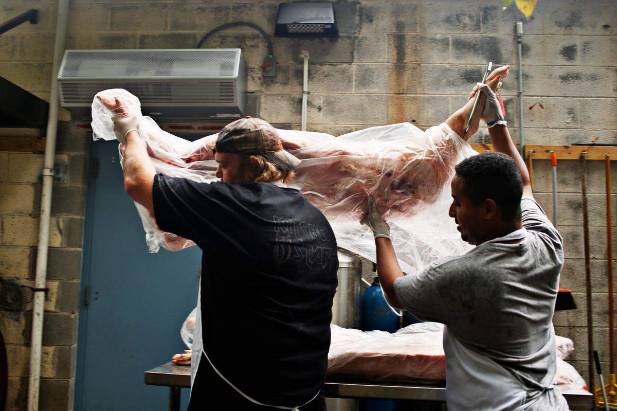 Daniel Bradford, left, and Methane Mihreteab, right, carry in a fresh hog from Green Button Farm at Picnic in Durham.