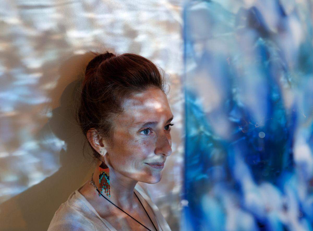 Sam Nguyen, owner of Say It With Glass, is photographed through a sheet of glass at her business in Carrboro, N.C. on Thursday, Nov. 7, 2024.