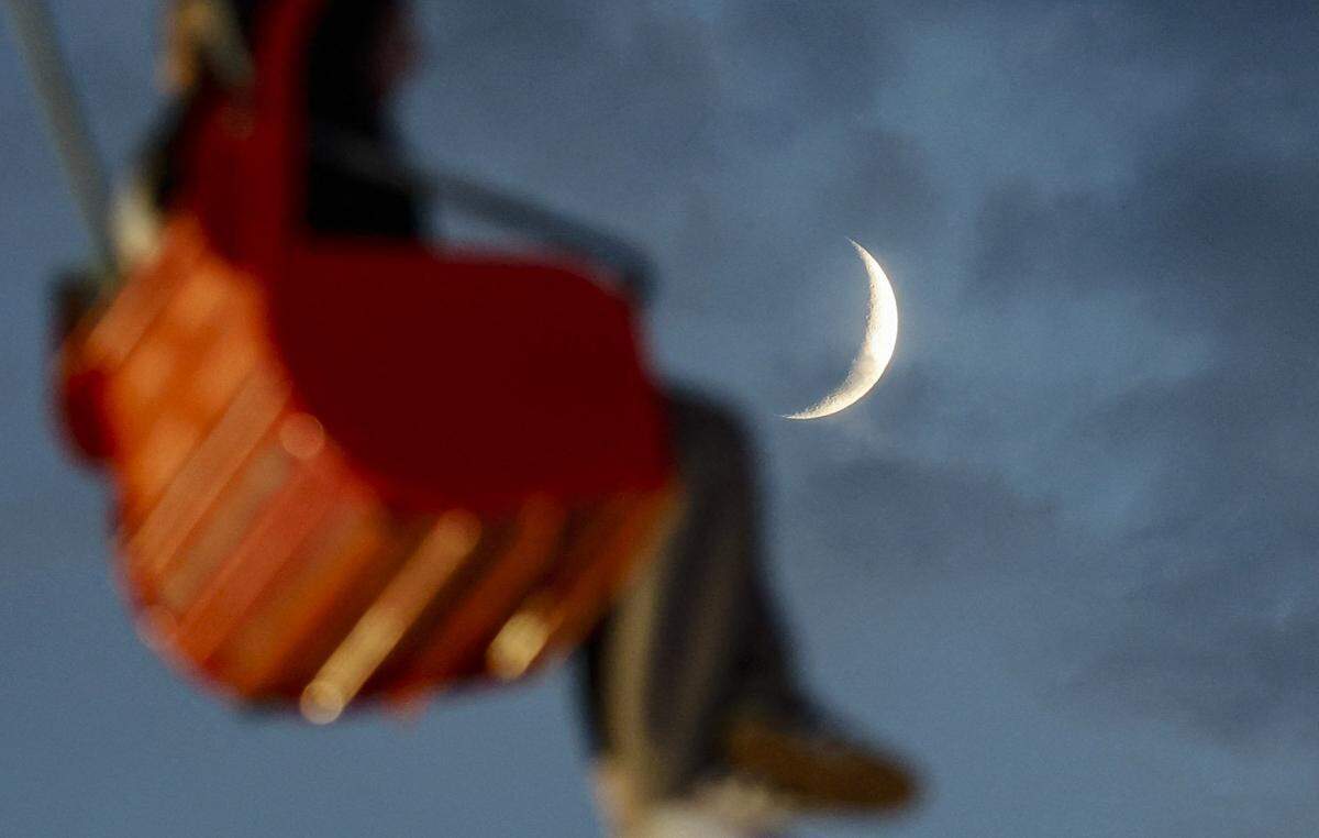 The moon peeks behind riders on the State Fair Flyer at the N.C. State Fair in Raleigh, N.C., on Saturday, Oct. 25, 2025.