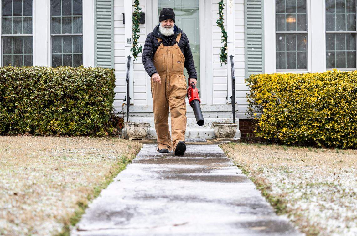 Nate Perry, of Graham, uses an electric leaf blower to clear a dusting of snow from his sidewalk as flurries begin falling Friday afternoon, Jan. 10, 2025.