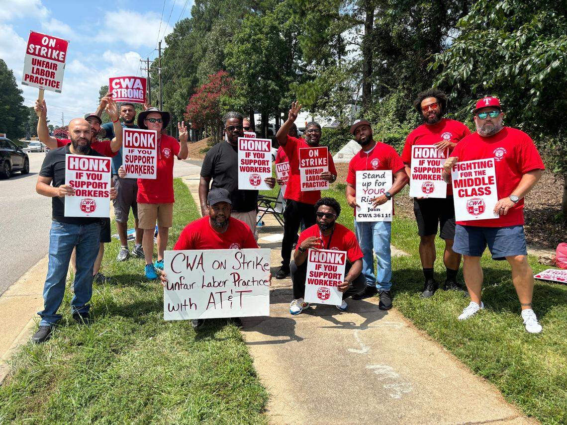 AT&T workers hold up signs and three fingers to represent District 3 of the Communications Workers of America union on Aug. 17, 2024 in Morrisville, NC