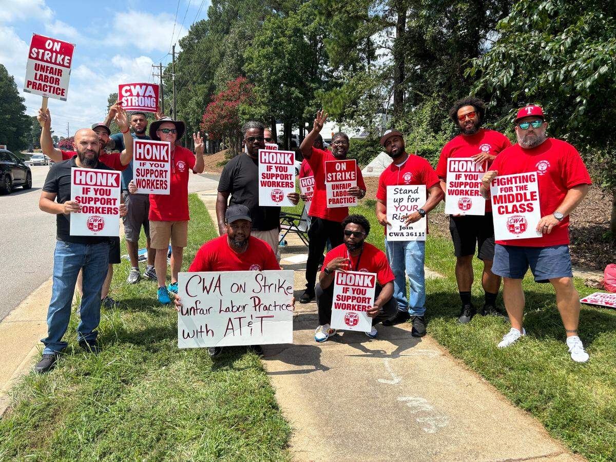 AT&T workers hold up signs and three fingers to represent District 3 of the Communications Workers of America union on Aug. 17, 2024 in Morrisville, NC