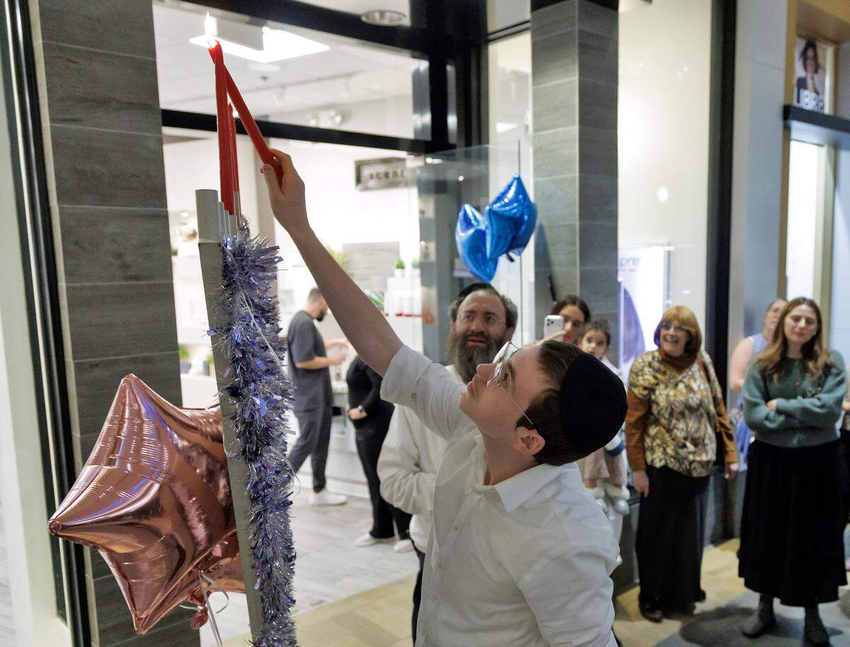 Hatomim Sholom Bluming lights a menorah during an event hosted by Chabad of Durham-Chapel Hill at Skin Analytics at The Streets at Southpoint on Thursday, Dec. 18, 2025, in Durham, N.C. 