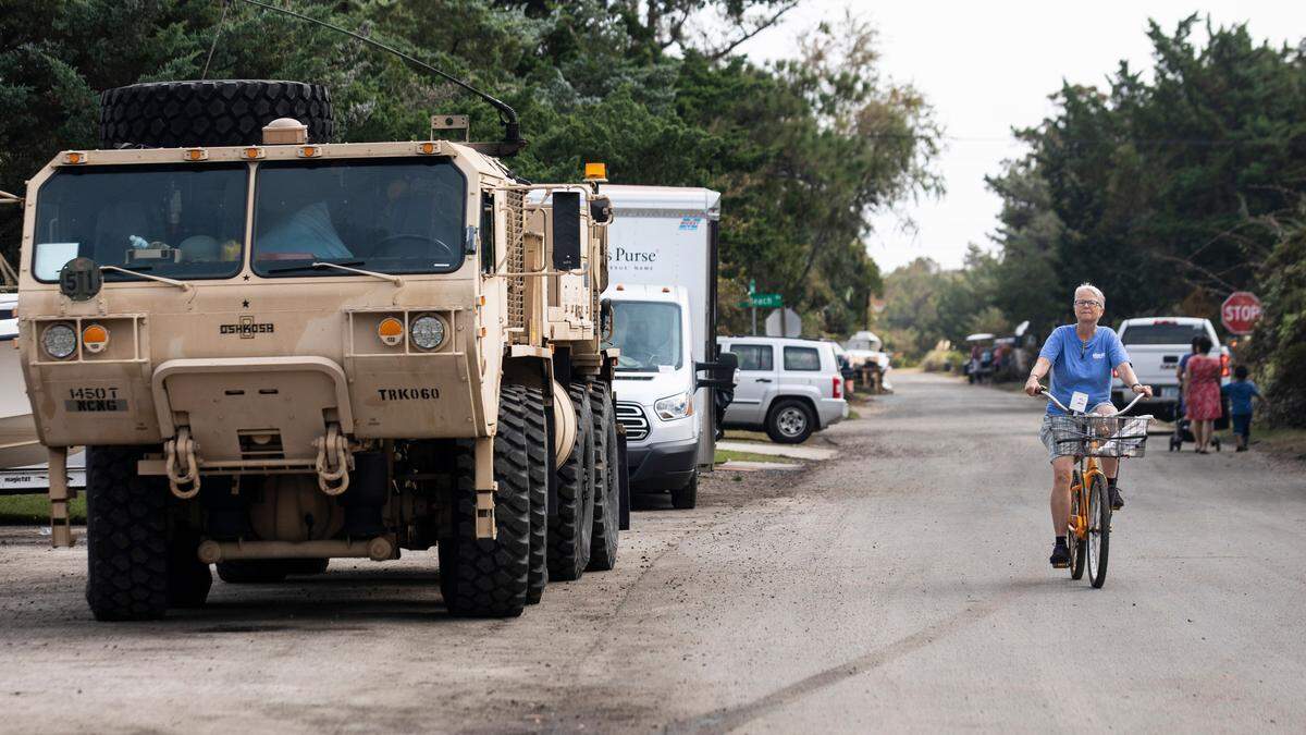 A woman rides a bicycle past an N.C. National Guard vehicle outside the Pony Island Restaurant in Ocracoke, NC on Friday morning, Sept. 13, 2019.