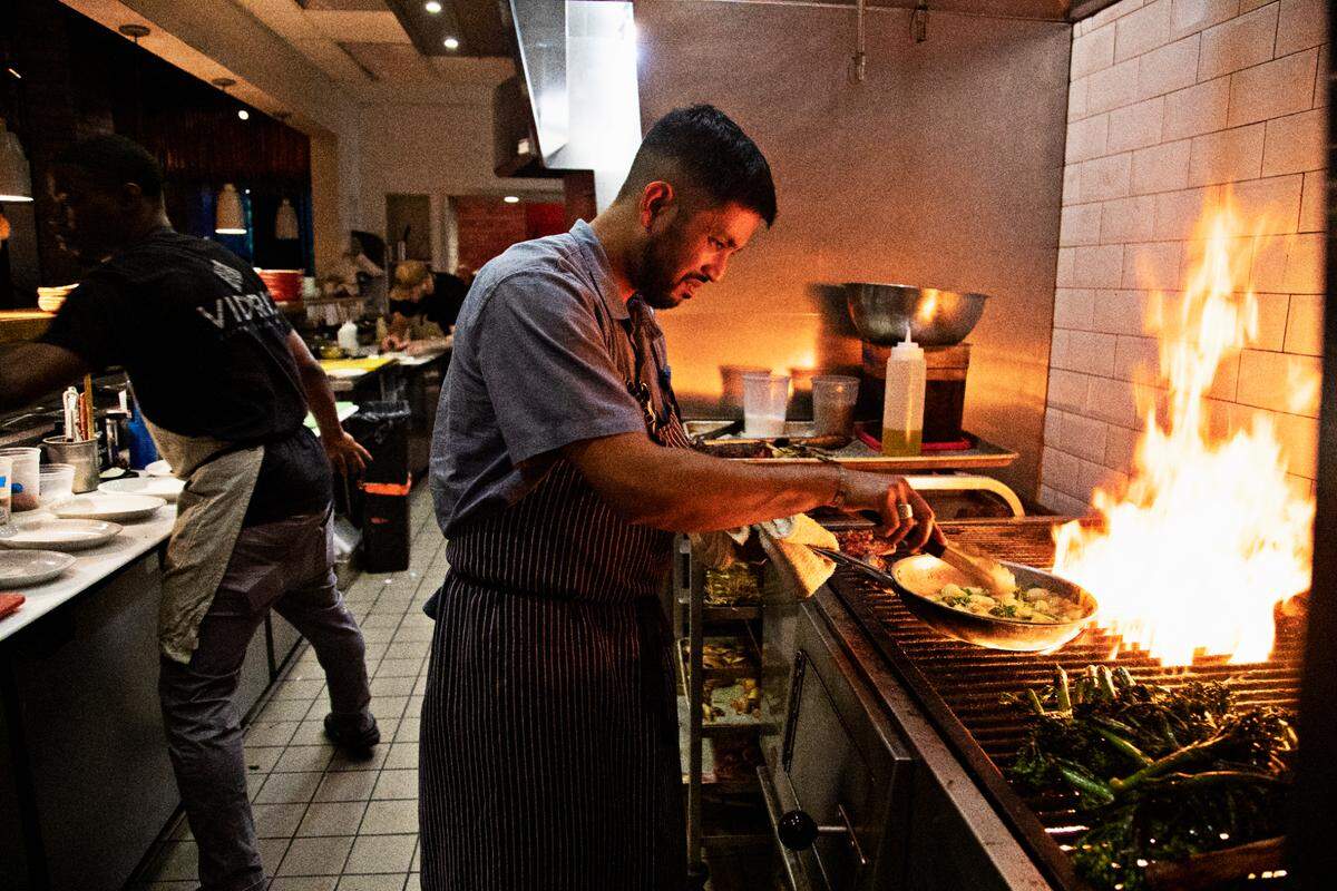 Vidrio chef Saif Rahman, right, makes a dish over the grill during dinner service on Tuesday, April 26, 2022, in the Raleigh restaurant. Rahman fasts for 14 hours daily during the month of Ramadan and is not able to break his fast until sundown which occurs during dinner service.