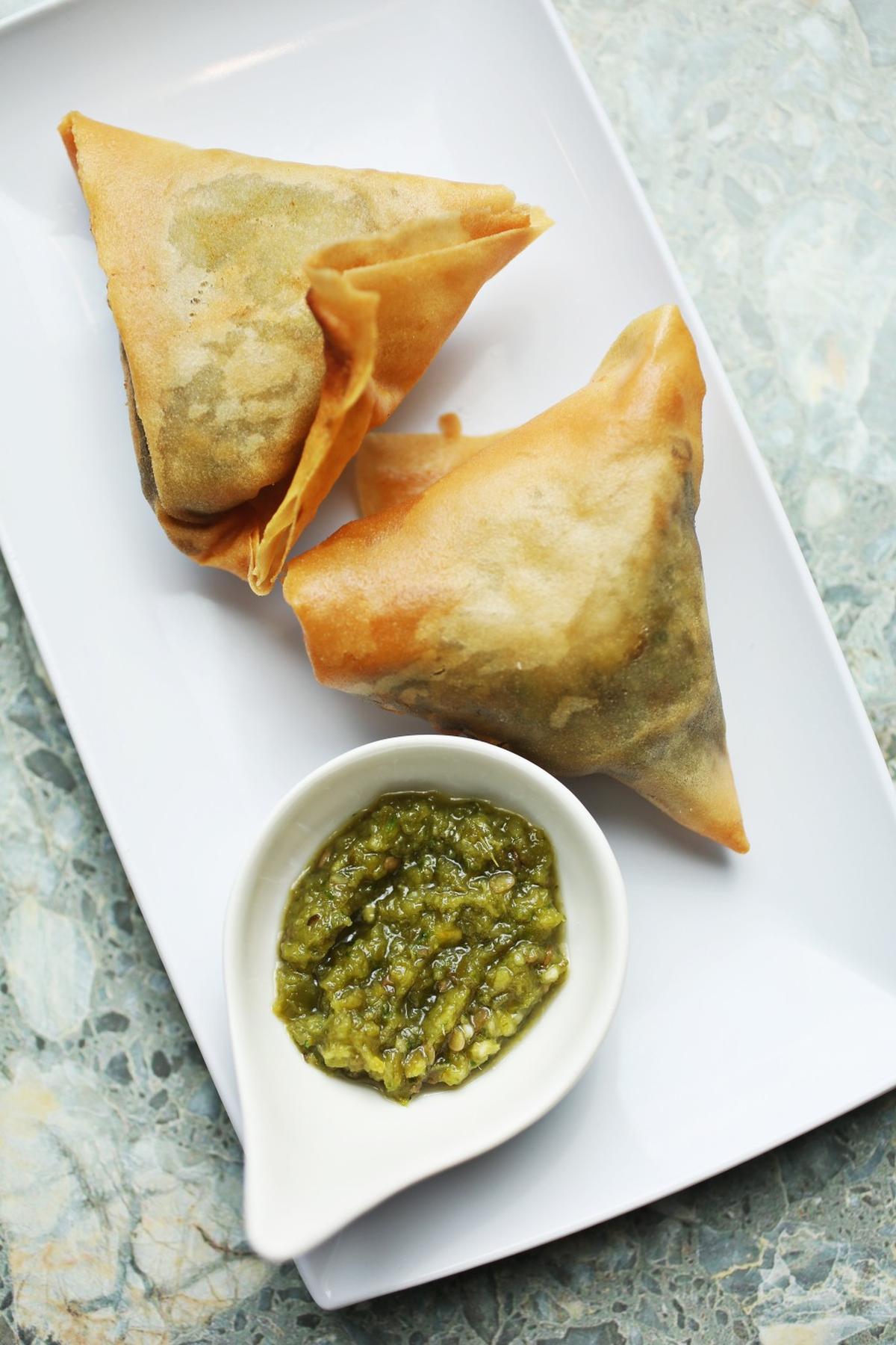 Goorsha's Sambusas are savory pastries with a filling of lentils, onions, garlic, and jalapenos wrapped in shatter-crisp phyllo that come with a pungent green sauce served in a sleek ceramic spoon of the sort used for tasting menus.