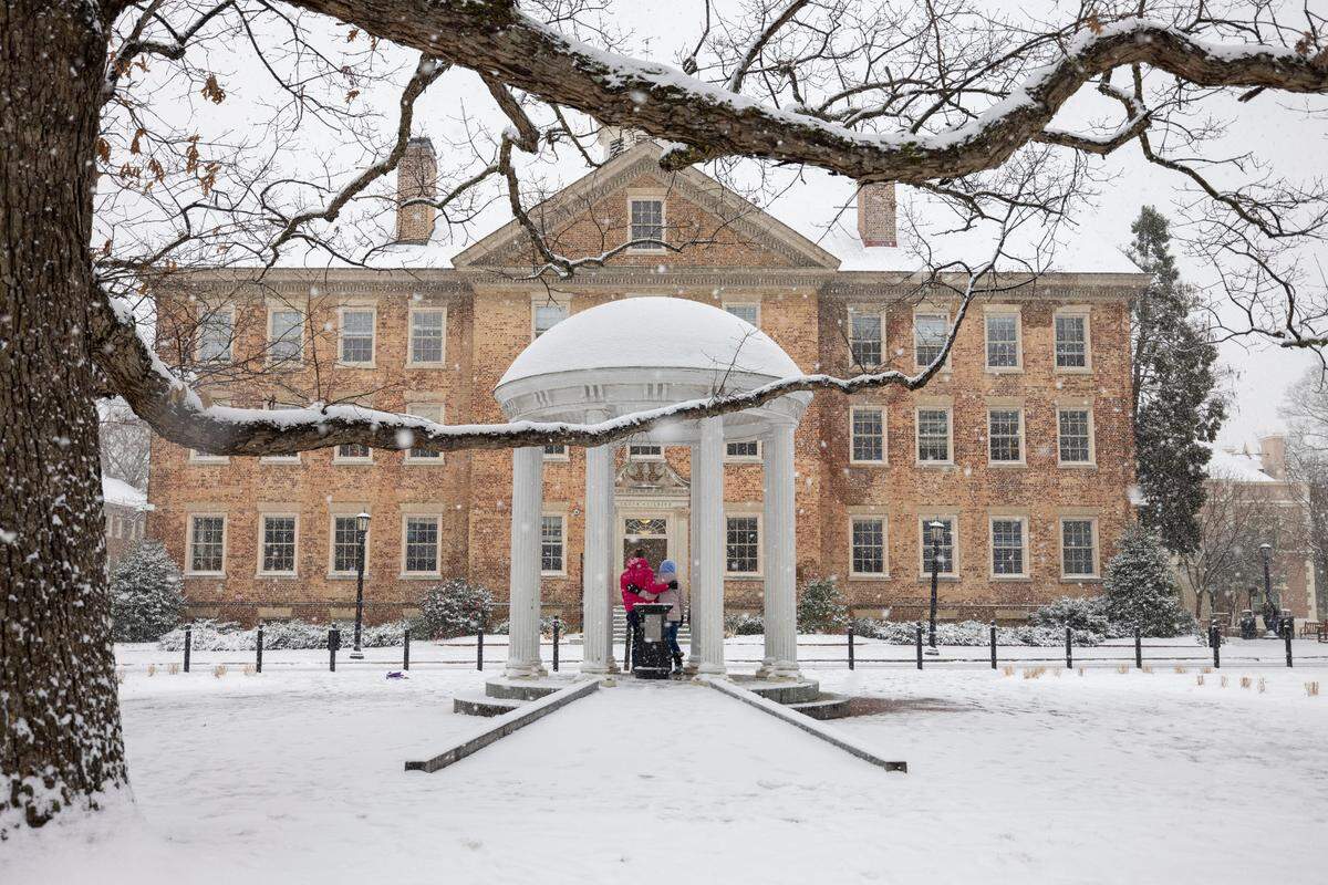 University of North Carolina students Ashton Jarman and Grace Glasgow pose for a photograph at the snow covered Old Well on campus as a winter storm moves through the area on Wednesday, February 19, 2025 in Chapel Hill, N.C.