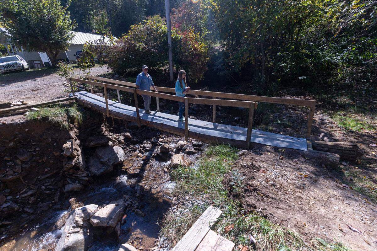 Dale Smith, 71, and Miranda Honeycutt, 11, walk across a makeshift bridge in Cruso on Saturday, October. 5, 2024 after a torrent of mud from a landslide destroyed the bridge leading to their property. The remnants of Hurricane Helene caused more than 300 landslides, many in North Carolina.