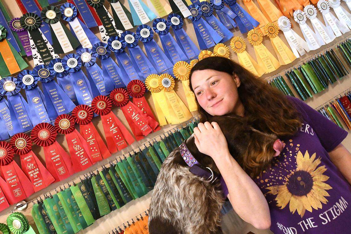 Ariel Wolf of Charlotte has learned to train medical service dogs, like her task-trained companion, Jubilee. Behind them, her set of awards is displayed. In Ariel’s free time, she competes with Jubilee and her other animals.