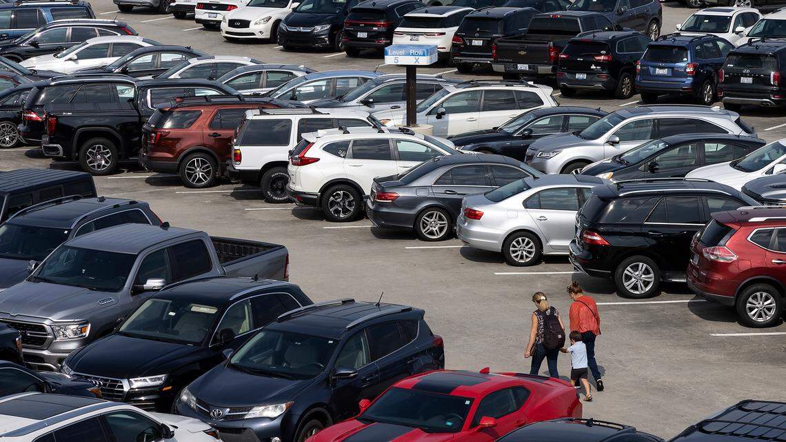 People walk through rows of vehicles in a parking lot.