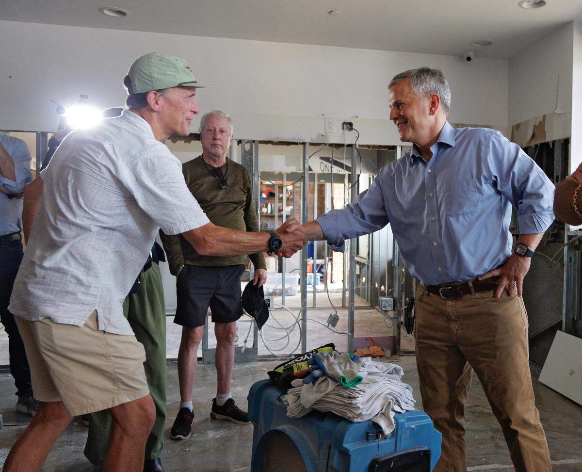 N.C. Gov. Josh Stein shakes hands with Chuck Millsaps, president and owner of Great Outdoor Provision Co., during a tour of flood damage caused by remnants of Tropical Storm Chantal at Eastgate Crossing in Chapel Hill, N.C.