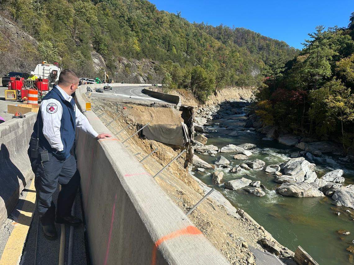 A Haywood County sheriff’s deputy looks over the median barrier on Interstate 40 toward the missing eastbound lanes in the Pigeon River Gorge. Photo taken Oct. 17, 2024, when U.S. Transportation Secretary Pete Buttigieg visited places damaged by the remnants of Hurricane Helene.