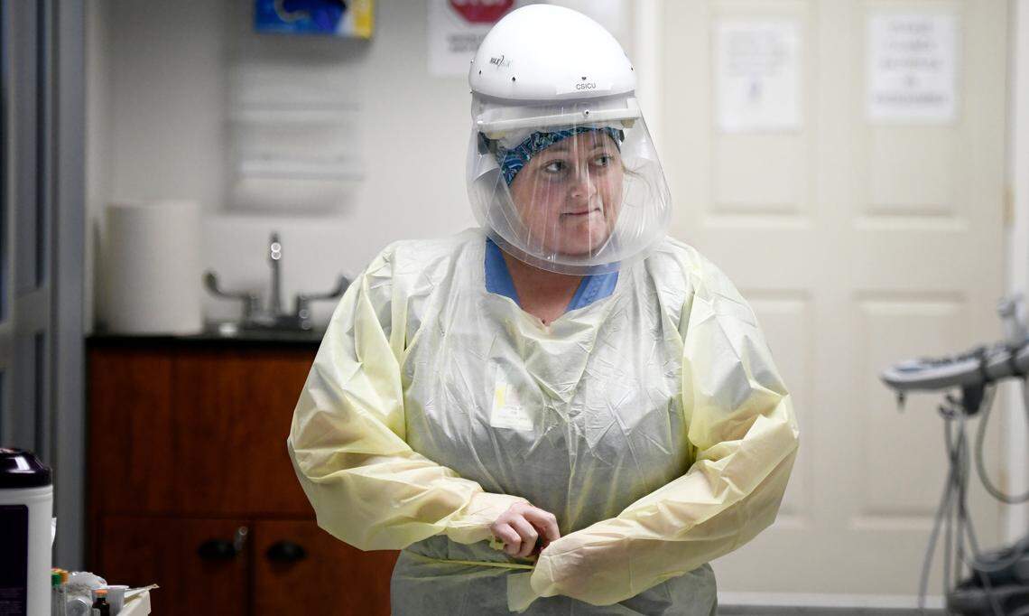 April Mangum, RN, ties a protective gown as she prepares to enter the room of a coronavirus patient in the the Special Respiratory Isolation intensive care unit at UNC Rex Hospital Wednesday, May 6, 2020. She is wearing a protective MaxAir which incorporates an air purifying respirator with a sealed face shield.