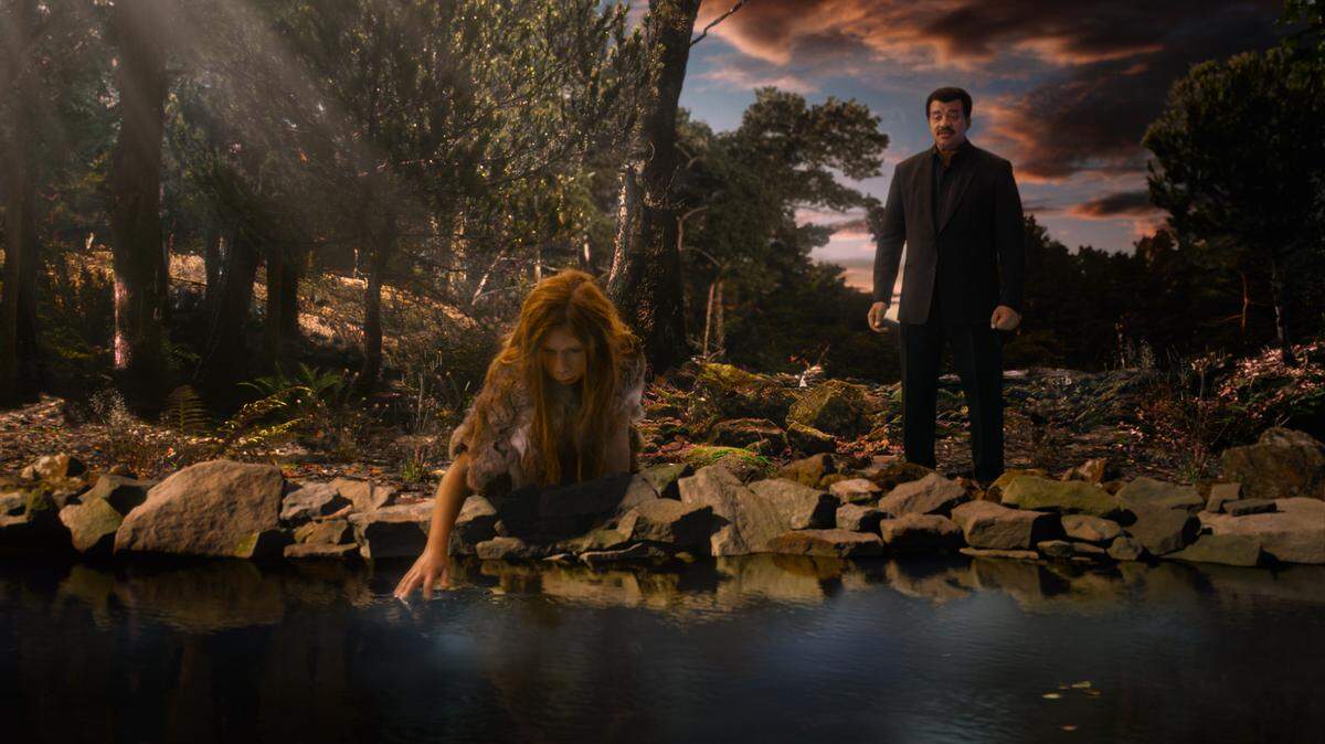 A young Neanderthal girl kneels at the water’s edge as host Neil deGrasse Tyson looks on in “Cosmos: Possible Worlds,” premiering March 9, 2020, on the National Geographic channel.
