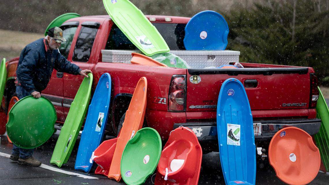 Johnny Howard places plastic sleds and snow discs around his pickup truck as snow begins to fall in Pittsboro, Friday afternoon, Jan. 10, 2025. Howard was selling the sleds to customers hoping for sledding weather.