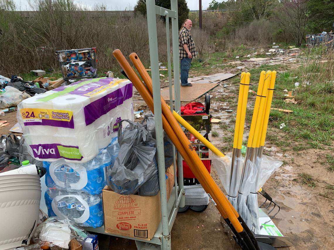 Michael Kelly, a street outreach specialist for Triangle Family Services, surveys a homeless camp off Capital Boulevard and Interstate 540 on Friday. In the foreground are shovels, rakes and other cleaning supplies that residents and volunteers will use to begin cleaning up the site.