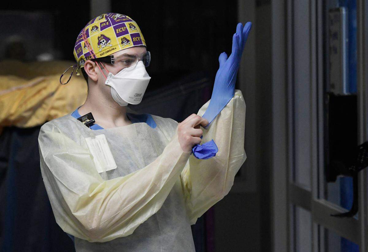 Jonathan Vitek dons rubber gloves before entering the room of a COVID patient Thursday, March 25, 2021.