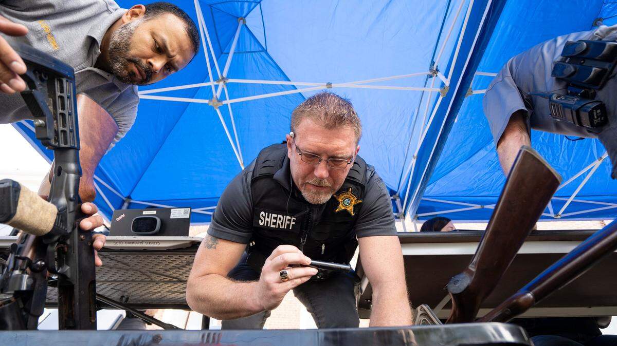 Luis Patino and R.J. Christie with the Durham County Sheriff’s Office sort through a box of guns turned in at a gun buyback event in Durham, N.C. on Saturday, Aug. 6, 2022.