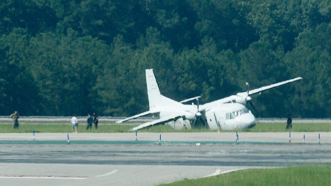 A twin-engine turbo prop aircraft sits on the grass near runway 5R-23L at Raleigh-Durham International Airport Saturday July 30, 2022. The plane made an emergency landing at RDU Friday after reporting landing gear issues.