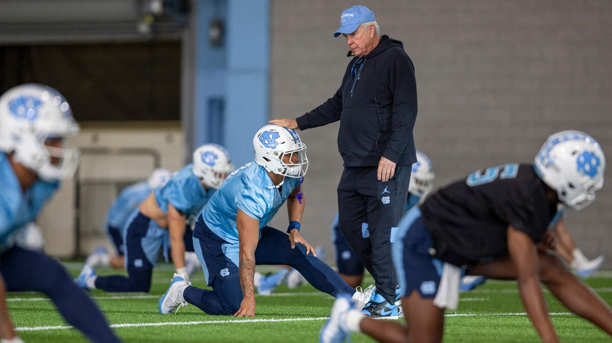 North Carolina coach Mack Brown gives Caleb Hood (4) a pat on the head as he stretches during the opening day of their spring football practice on Tuesday, March 19, 2024 in Chapel Hill, N.C.