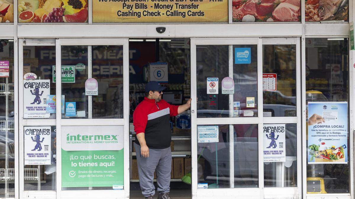 A security guard operates an automatic sliding door while watching the parking lot outside the International Foods grocery on New Hope Church Road in Raleigh on Wednesday, Nov. 19, 2025, after federal immigration enforcement agents were seen circulating the area in unmarked SUVs. Immigrant rights groups said federal agents detained at least 12 Triangle residents on Tuesday, including in Raleigh, Durham and Cary.