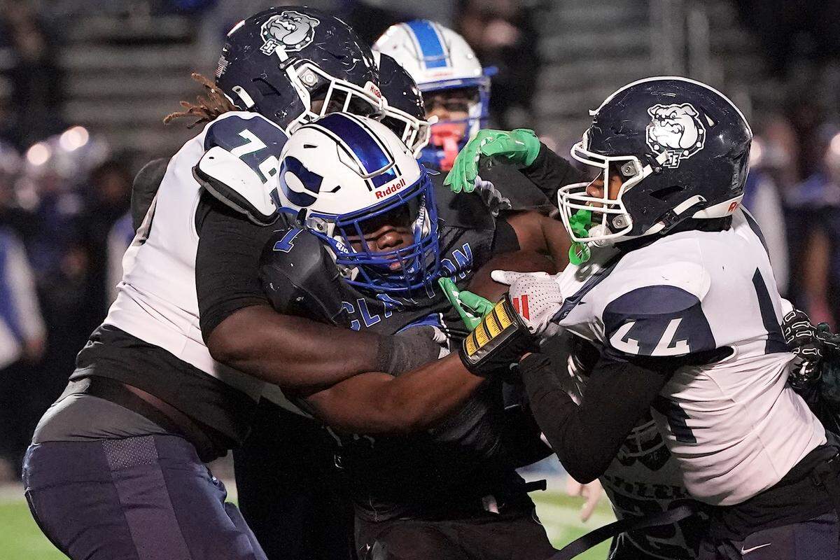 Clayton running back Noah Smith (1) is tackled by Southeast Raleigh defensive lineman Grayson Williams (79) and linebacker Cyrus Gunther during the first half. The Clayton Comets and the Southeast Raleigh Bulldogs met in the fourth round of the NCHSAA 7A Playoffs in Clayton, N.C. on Nov. 28, 2025.
