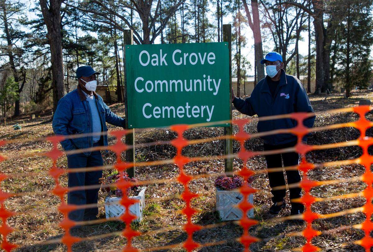 Albert Crenshaw, left, and John Goode stand for a portrait with the sign for the Oak Grove Cemetery, which was founded by freed African-Americans after the Civil War and now has lost more of its tree buffer to widening of the I-440 Beltline, that separated it from the rest of the Method community in the 1960s, on Wednesday, Feb. 17, 2021, in Raleigh, N.C.