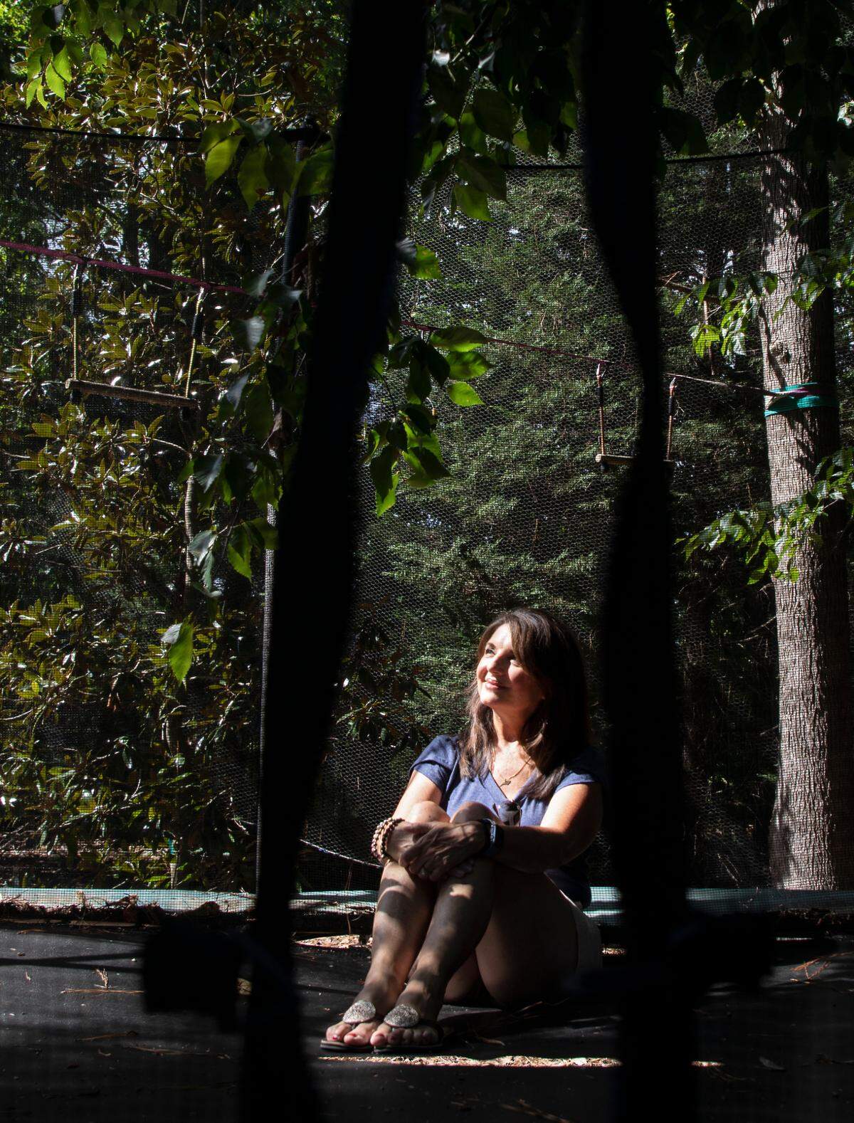 Sharon McCloud sits on a trampoline in the backyard of her Raleigh, N.C. home on Monday, August 8, 2022. After applying to have a trampoline in her yard in the fall of 2020, McCloud says she was initially told she’d have to get approval from her neighbors on its placement, despite having a play set in the same spot for 15 years. After documenting other trampolines in the neighborhood and speaking with neighbors about their experiences, the HOA approved her request.