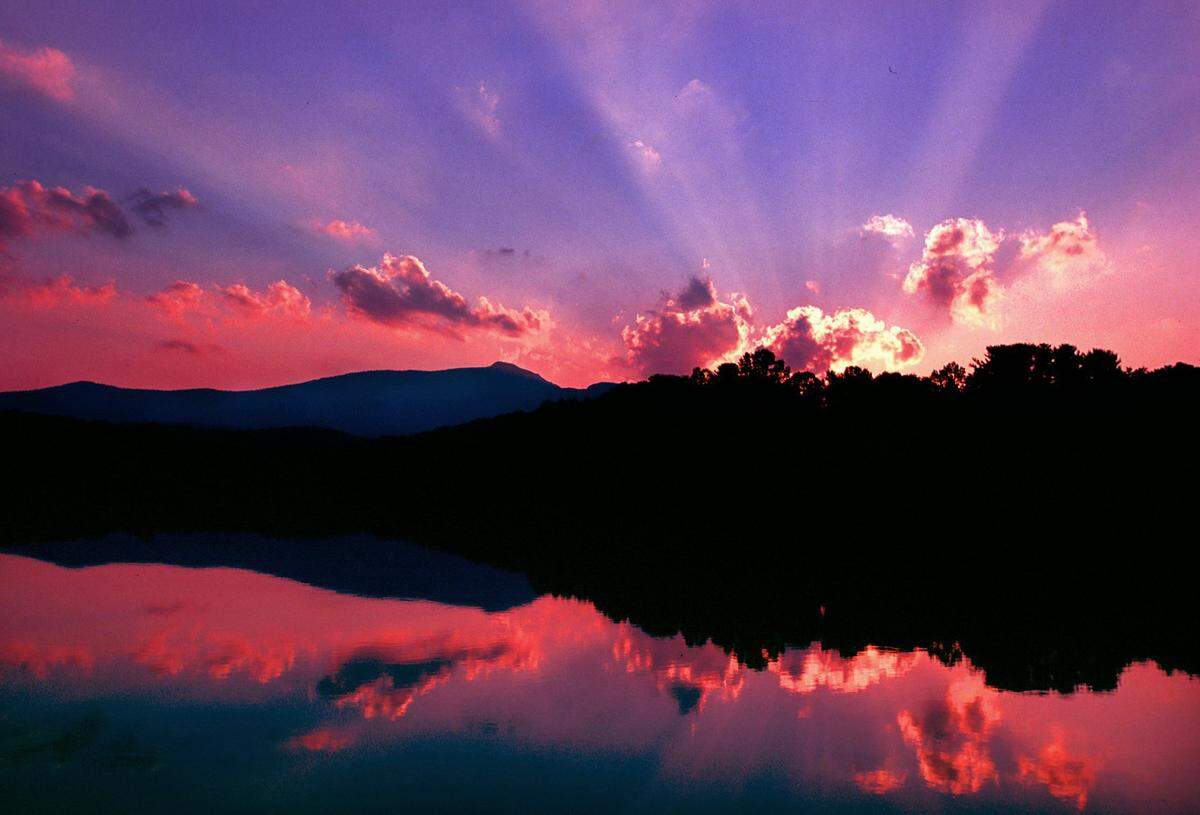 The sun sets at Price Lake near Boone, NC on the Blue Ridge Parkway in northwestern North Carolina as storm clouds move in over Grandfather Mountain.