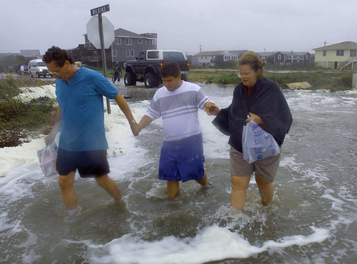 Sally and Phillip Adams of Richmond, Virginia, walk down a flooded section of Highway 12 in Kitty Hawk, NC, with son Brian, 18, as heavy surf churned over dunes eroded by the constant pounding of Hurricane Dennis in 1999.