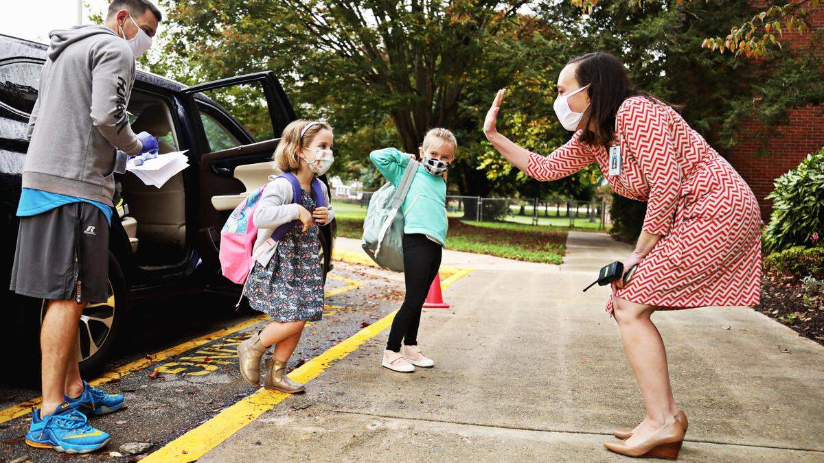 Hunter Elementary School principal Briana Pelton, right, gives an air high five to students after their health screening during drop-off in Raleigh on Monday, October 26, 2020, on the first day back in school for some Wake students.