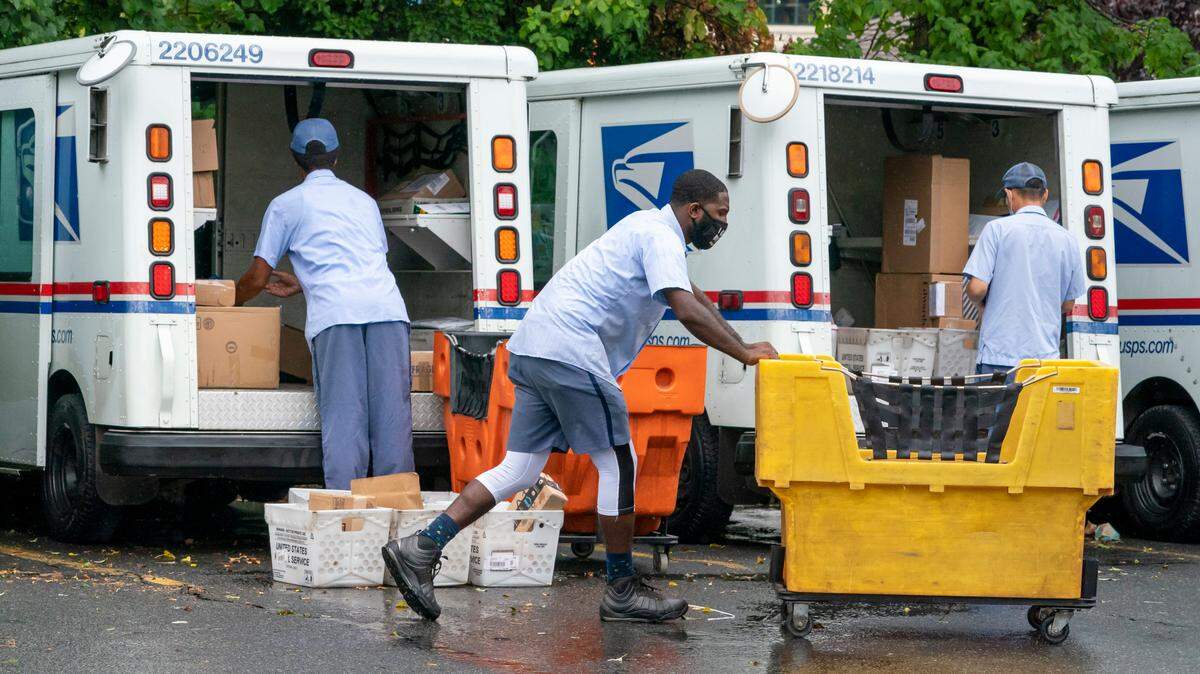 Letter carriers load U.S. Postal Service trucks in Virginia. Postmaster General Louis DeJoy said earlier this month that his plan to slow First Class mail and hike rates will help the USPS avoid bigger financial deficits and eroding service in the future.