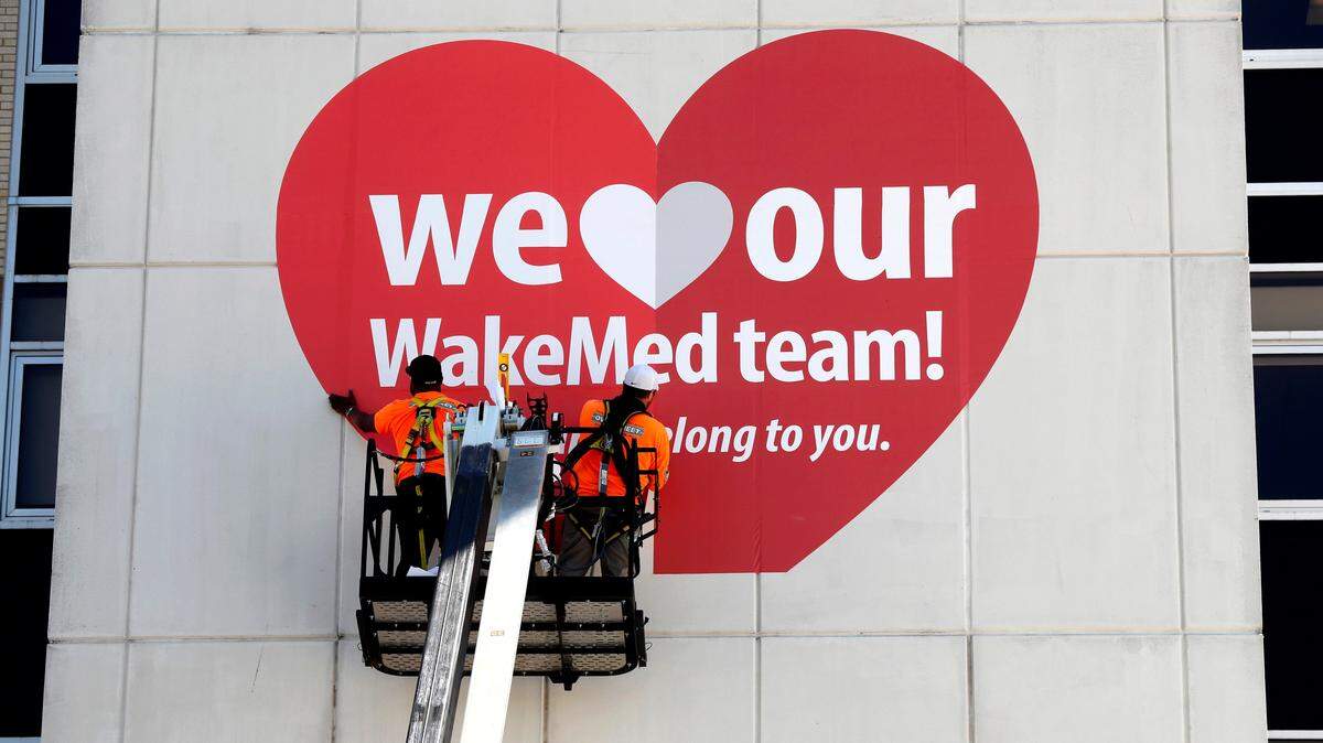 Shaun Johnson, left, and Steven Cooley with Overstreet Sign Contractors, put up a 18.75 foot wide and 15 tall heart over the entrance to the emergency department of Raleigh’s WakeMed hospital Wednesday, April 8, 2020.