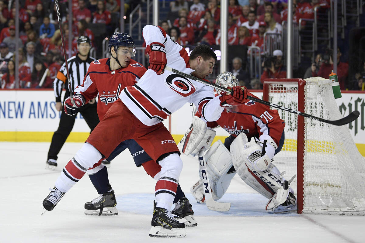 Carolina Hurricanes left wing Jordan Martinook, front, swings at the puck against Washington Capitals defenseman Dmitry Orlov, left, of Russia, and goaltender Braden Holtby (70) during the first period of Game 2 of an NHL hockey first-round playoff series, Saturday, April 13, 2019, in Washington. (AP Photo/Nick Wass)