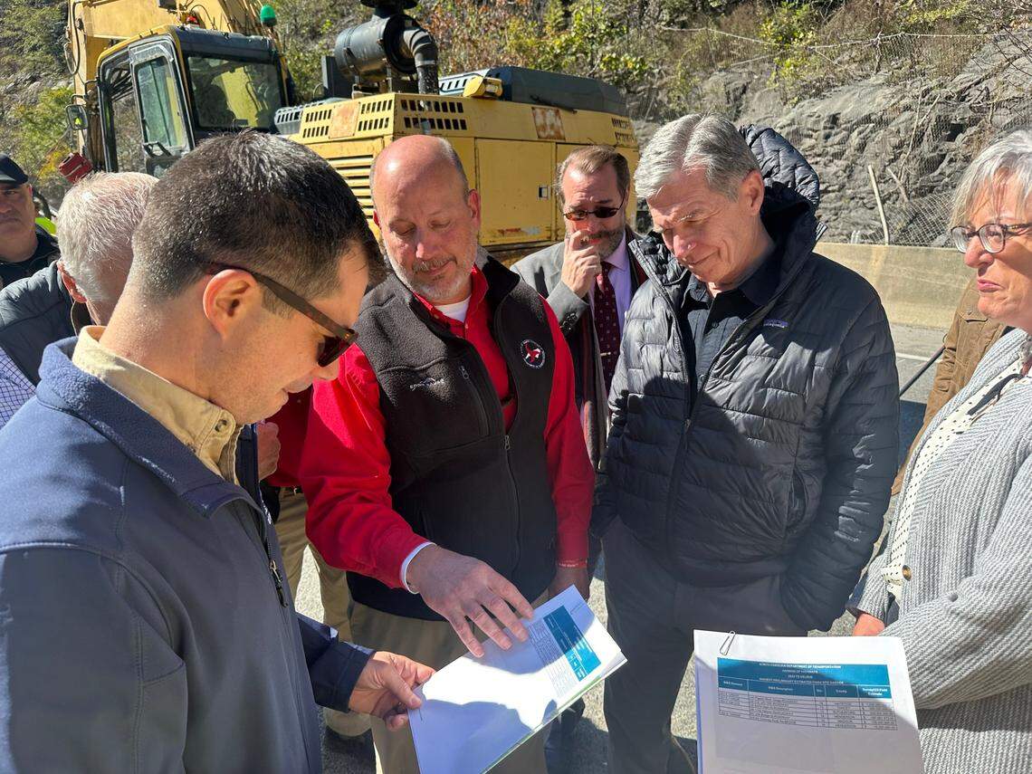 N.C. Transportation Secretary Joey Hopkins presents a list of the biggest road reconstruction projects after Hurricane Helene to U.S. Transportation Secretary Pete Buttigieg, left. Looking on during a visit to Interstate 40 in the Pigeon River Gorge are Gov. Roy Cooper and Wanda Payne, NCDOT’s top engineer in the region.