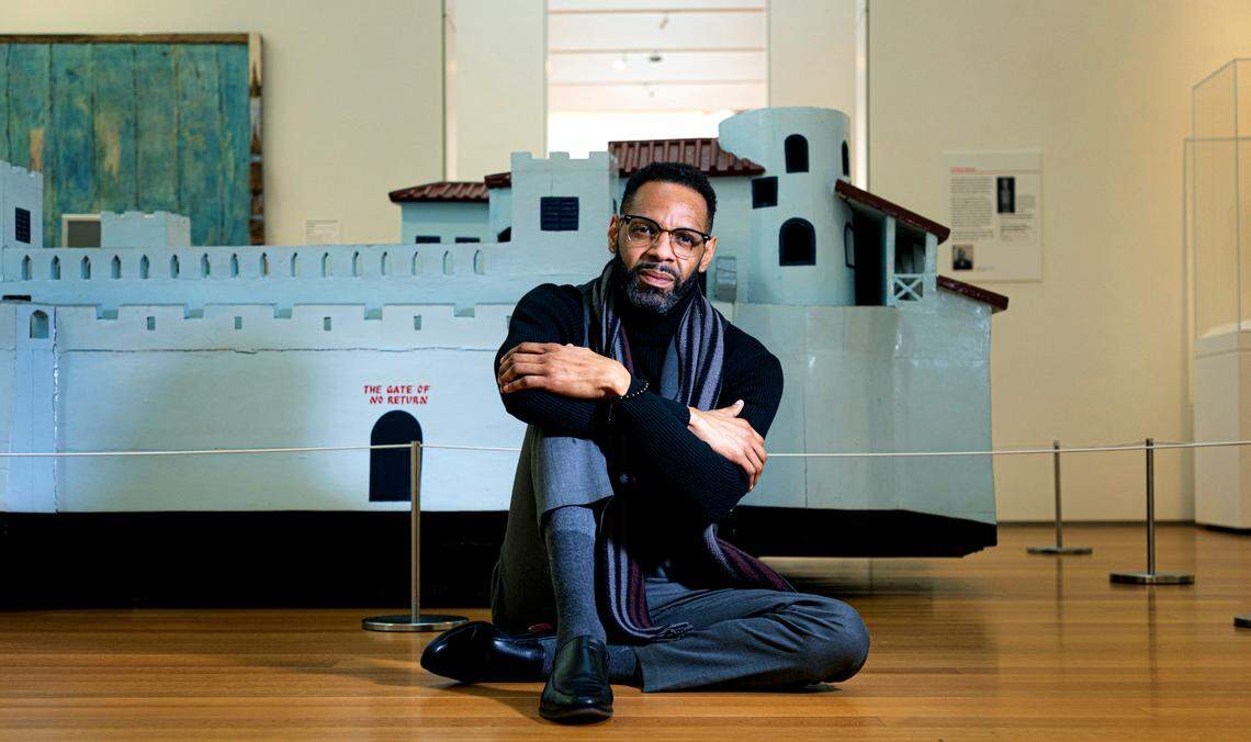 Moses T. Alexander Greene, the North Carolina Museum of Art’s director of performing arts and film, poses next to Joseph Tetteh Ashong’s Elmina Castle, a slave fort replica, inside the museum Tuesday, Feb. 7, 2023.