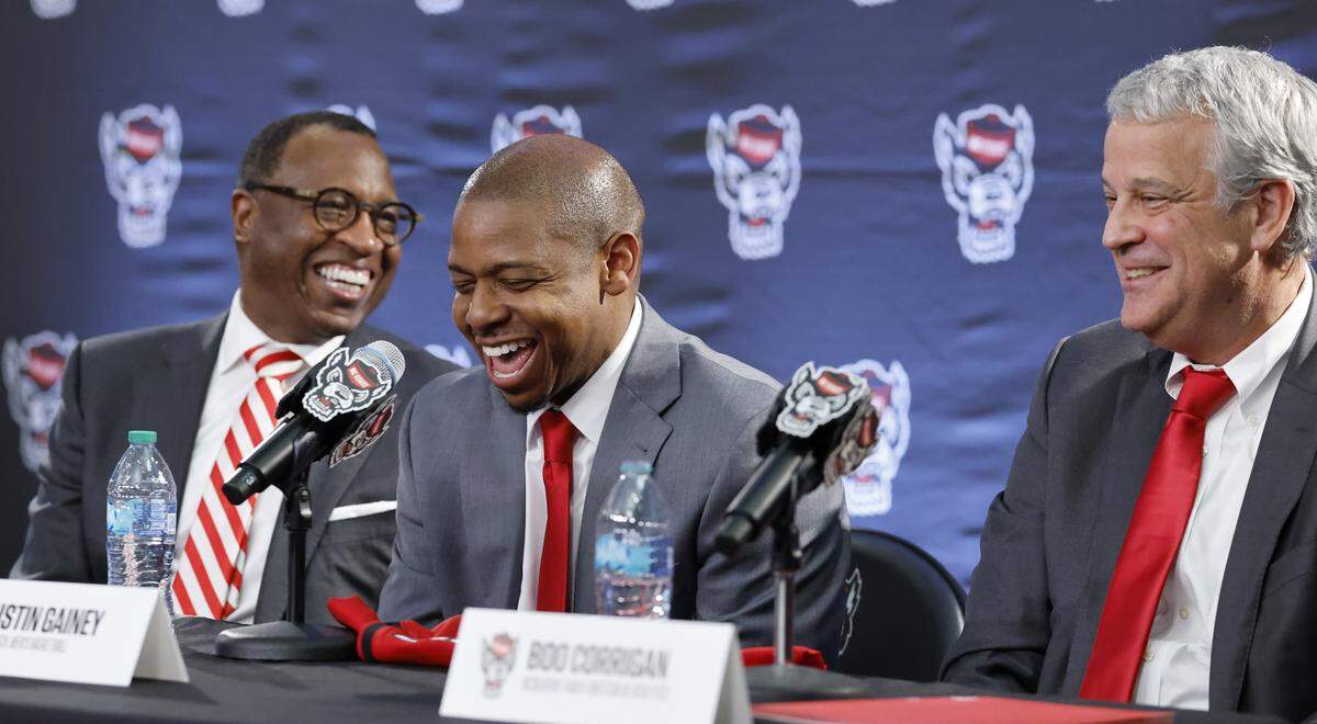 New N.C. State head men’s basketball coach Justin Gainey laughs at a statement by Athletic Director Boo Corrigan while sitting with Chancellor Kevin Howell during a press conference where Gainey was introduced as the new head coach at the Lenovo Center in Raleigh, N.C., Wednesday, April 1, 2026.