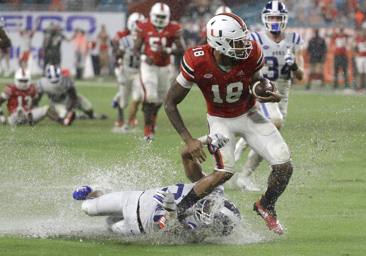 Miami wide receiver Lawrence Cager (18) escapes a tackle by Duke safety Brandon Feamster for a first down during the first half.