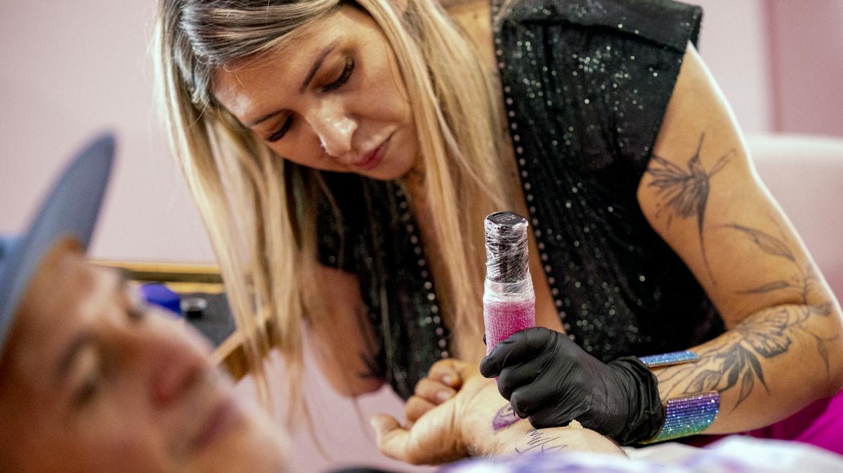 Camila Gama Marrache applies a tattoo to Dante Zambrano during the grand opening of her new studio, Beauty Art Studio, on Franklin Street in Chapel Hill on Saturday, Sept. 7, 2024. Marrache lost her right arm to a botched liposuction procedure last year.