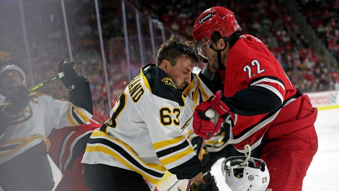 Boston Bruins center Brad Marchand (63) loses his helmet as he battles along the boards with Carolina Hurricanes defenseman Brett Pesce (22) during the third period of an NHL hockey game Thursday, Oct. 28, 2021, in Raleigh, N.C. (AP Photo/Chris Seward)