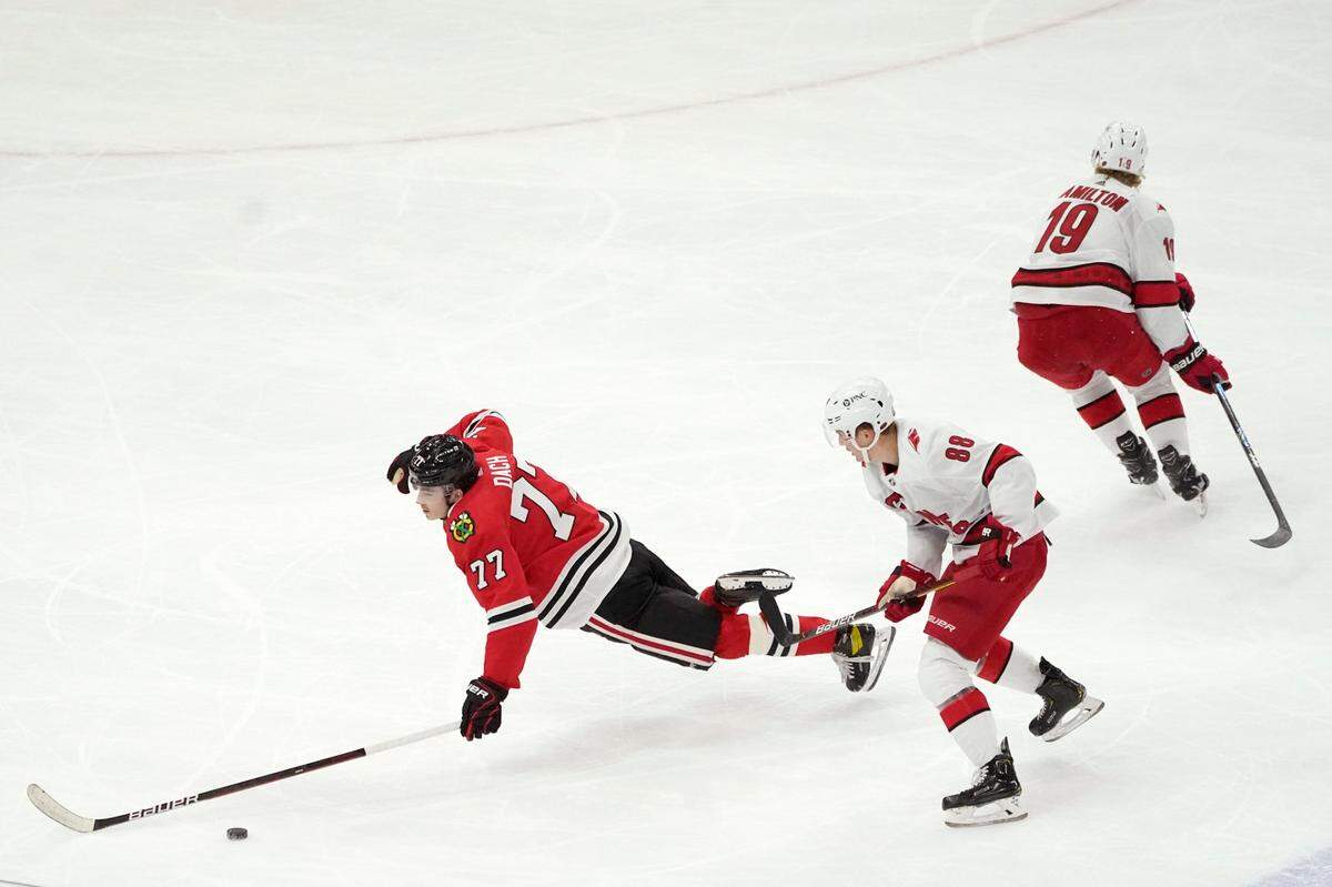 Chicago Blackhawks’ Kirby Dach, left, falls to the ice after being tripped by Carolina Hurricanes’ Dougie Hamilton (19) as Martin Necas (88) watches during the first period of an NHL hockey game Tuesday, March 30, 2021, in Chicago. (AP Photo/Charles Rex Arbogast)