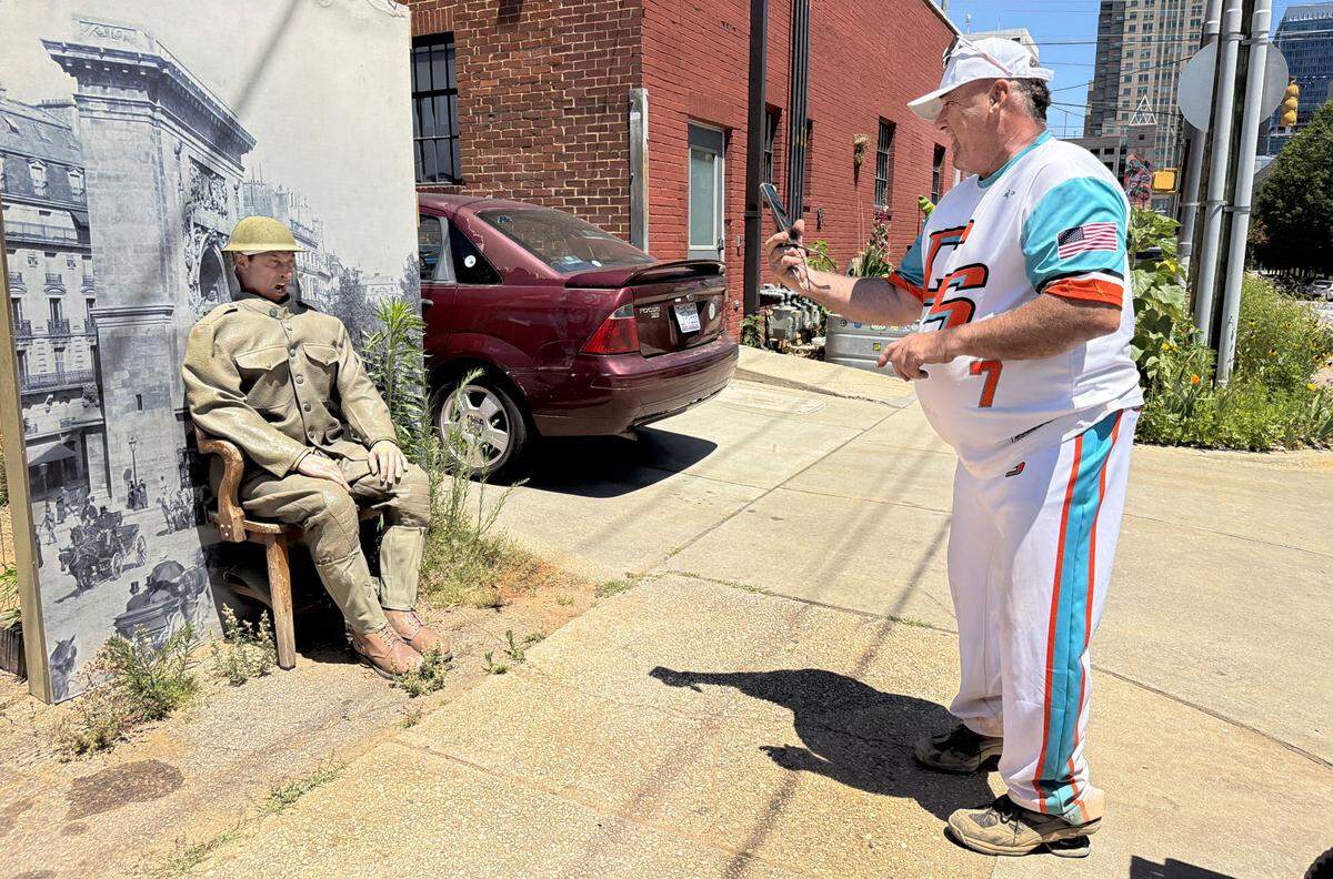 As Ralph Covello takes his photo, Frankie Vartuli poses in the World War I soldier display on West Cabarrus St. near S. Dawson St. in Raleigh, N.C., Friday, May 15, 2026. The display came from the N.C. Museum of History which is currently being renovated.