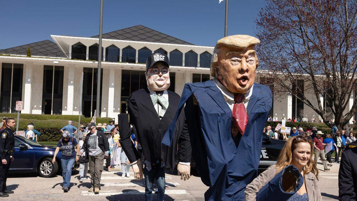 Large puppets of President Donald Trump and Elon Musk make their way across the street from the N.C. Legislature, Wednesday, March 12, 2025, following a protest in opposition to cuts and actions by DOGE and Elon Musk.