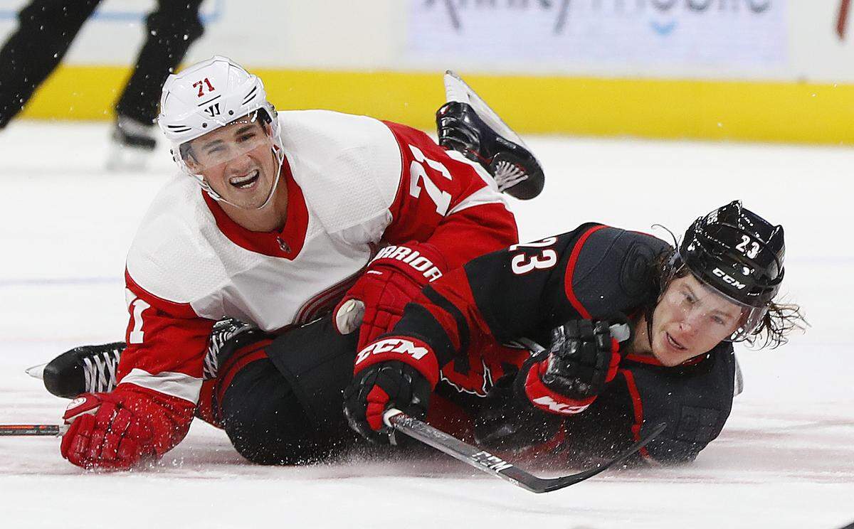 Detroit Red Wings center Dylan Larkin (71) and Carolina Hurricanes left wing Brock McGinn (23) hit the ice in the first period of an NHL hockey game Monday, Oct. 22, 2018, in Detroit. Larkin was called for a tripping penalty.