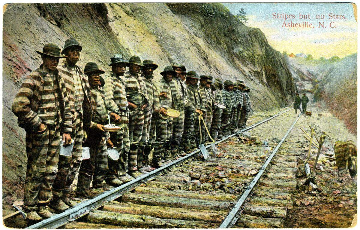 A postcard made from a photo of prison inmates working on the Western North Carolina Railroad, with two men with guns in the background. In the late 1870s, Black men mostly from the eastern half of the state were arrested, often on dubious charges, and sentenced to hard labor building the railroad in the Blue Ridge Mountains.