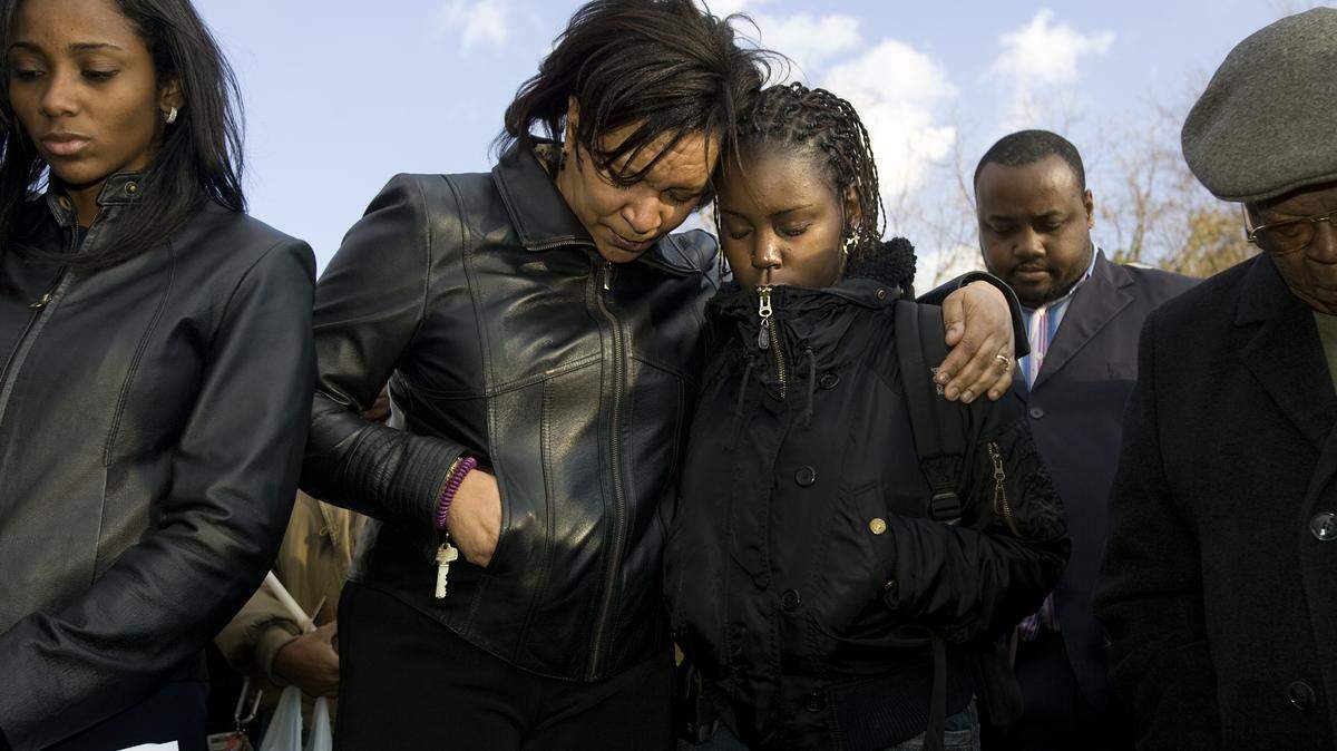 Family, community and St. Augustine College members gathered at the corner of Oakwood and N. Tarboro Street for a vigil for Adarius Fowler, 16, who was shot near the corner over the weekend. Crystal Roberts, assistant VP of Communications at St. Aug’s, center left, and K.K. Brice, a freshman at the school, center right, pray with others gathered for the event. Staff photo by Corey Lowenstein